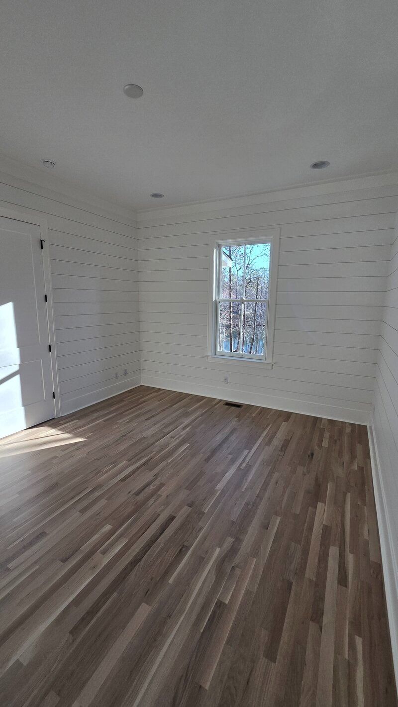 Empty room with wood floors and white shiplap walls, small window, and recessed lights.