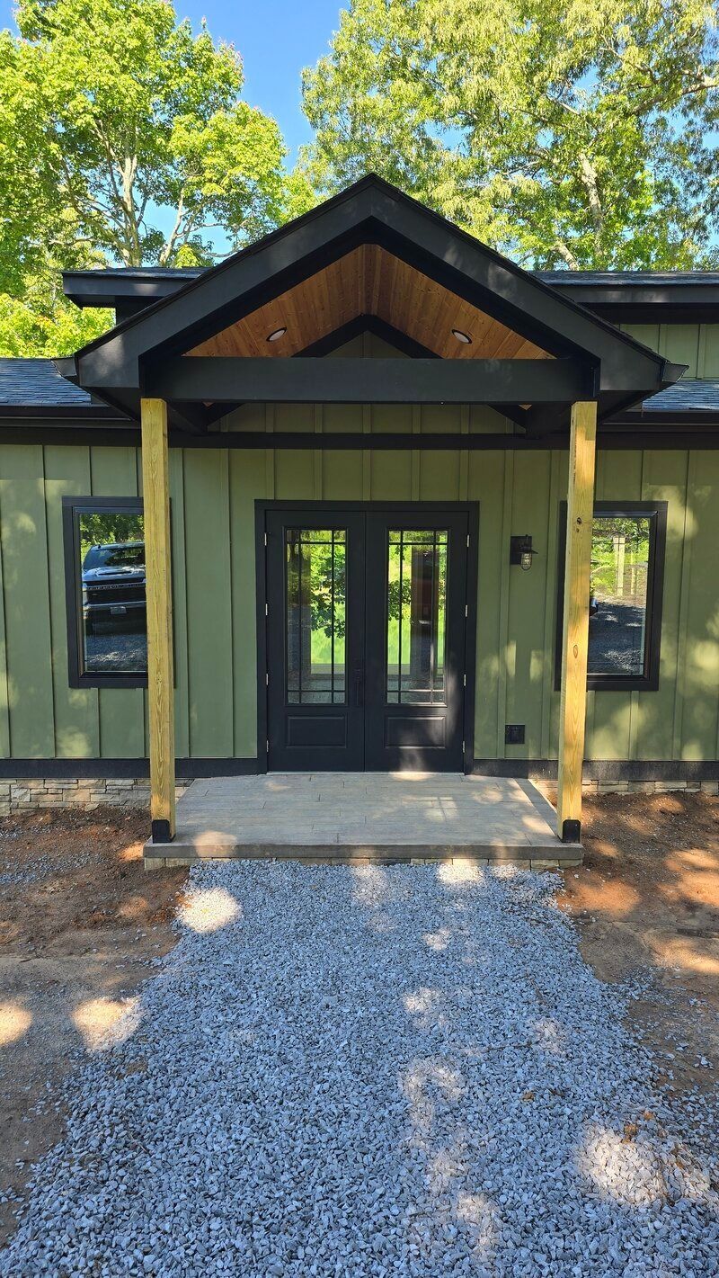Green cabin with black trim, double doors, and a gravel path leading to the entrance.