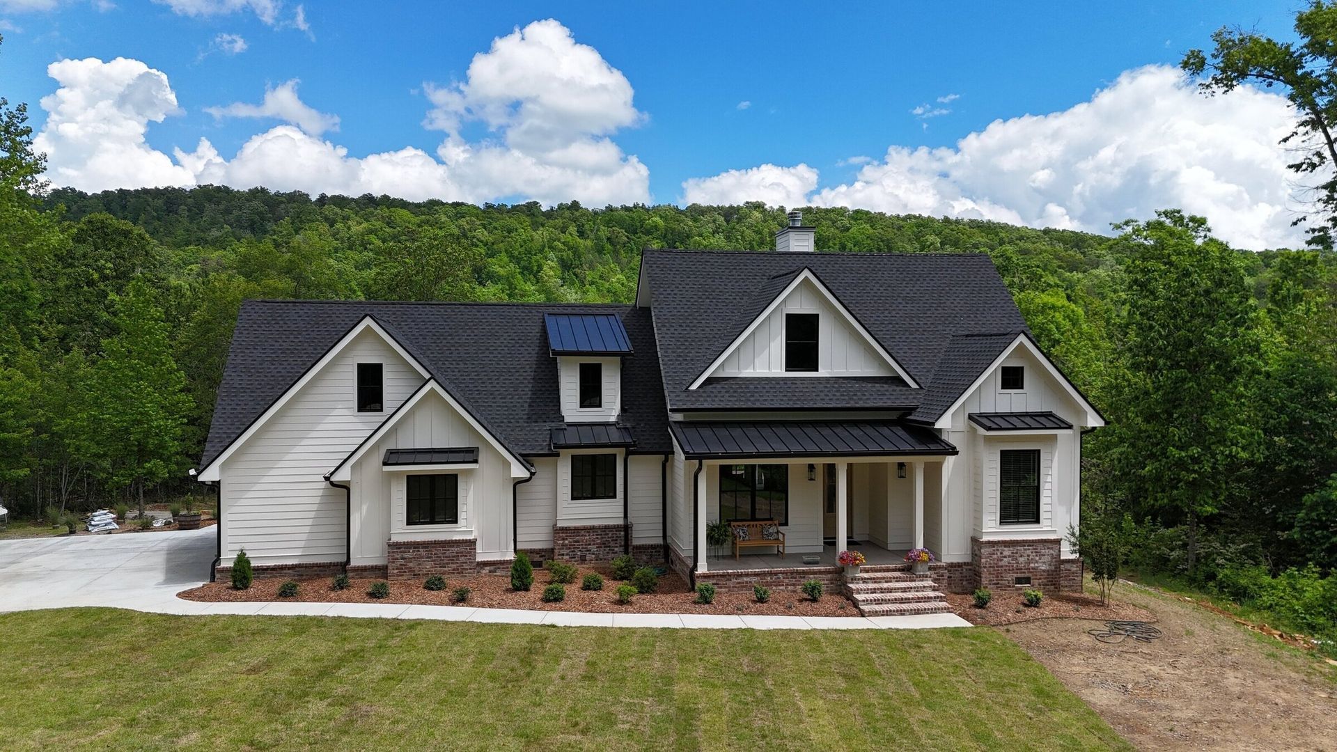 Craftsman-style home with gray roof, white siding, stone accents, green lawn, and trees under a blue sky.