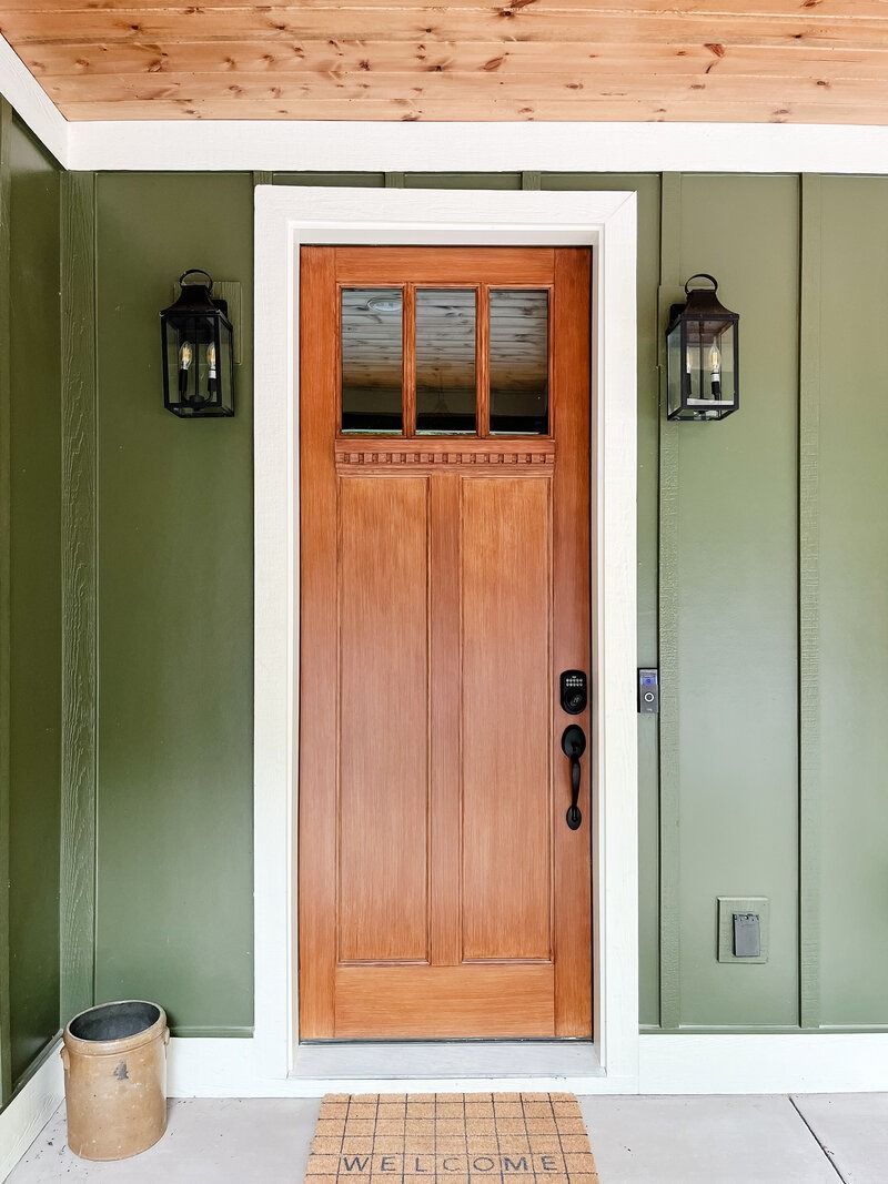 Wooden door with glass panes, flanked by black lanterns, set in a green paneled wall.