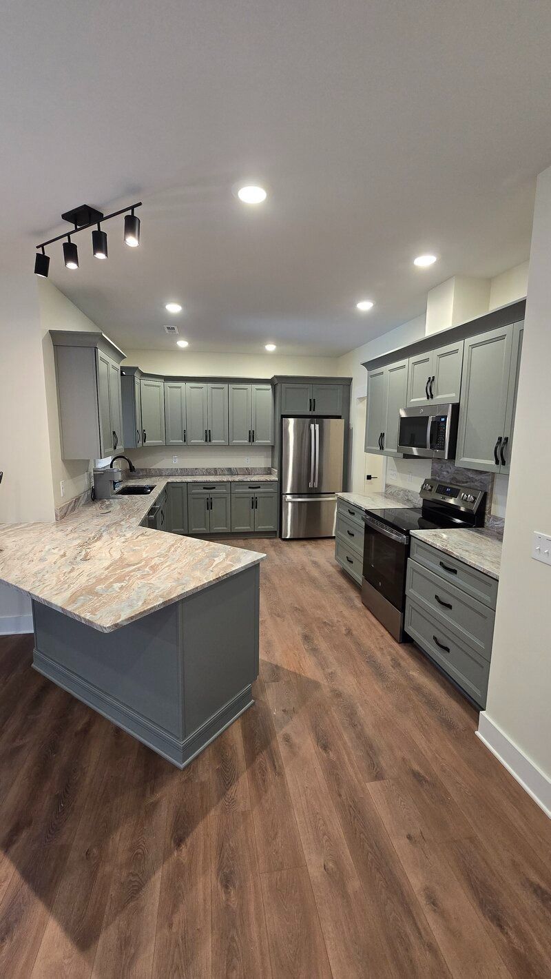 Modern kitchen with gray cabinets, island, stainless steel appliances, and wood-look flooring.