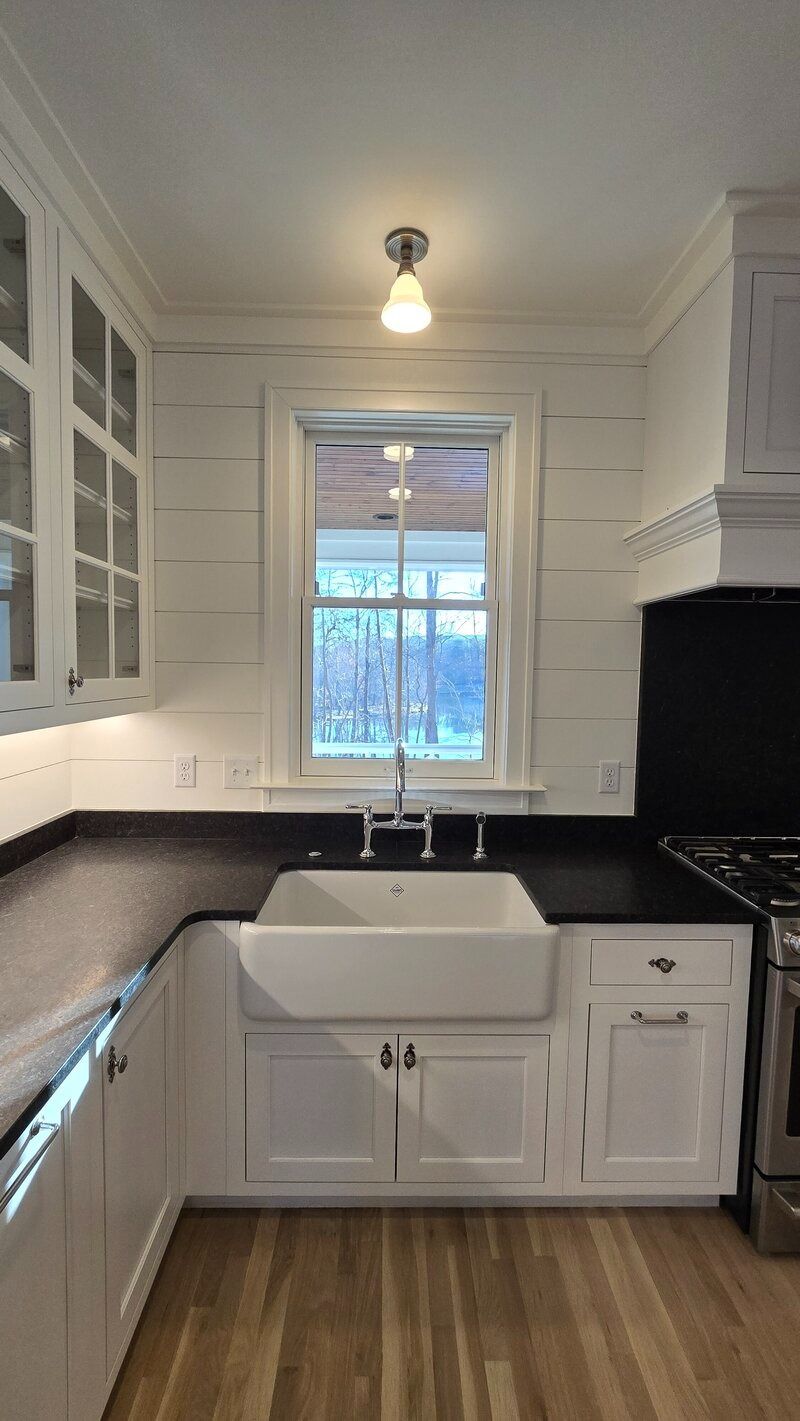 White kitchen with farmhouse sink, black countertops, and wood floor.