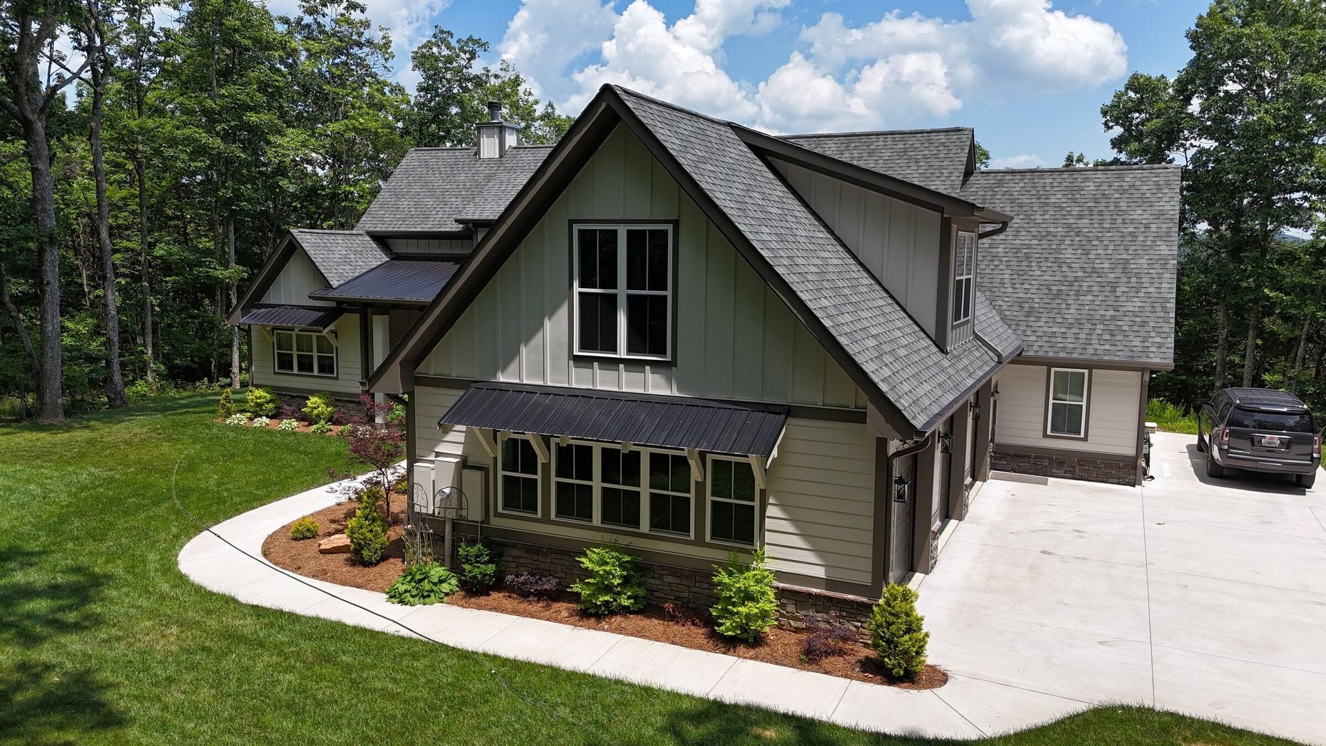 Two-story house with gray roof, green lawn, trees, and a car parked in the driveway.