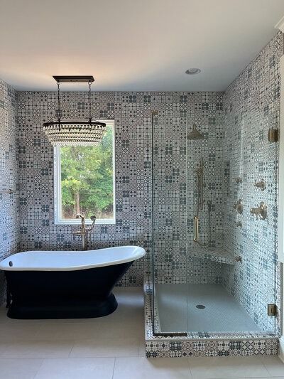 Bathroom with patterned tile walls, a dark clawfoot tub, glass shower, and chandelier.