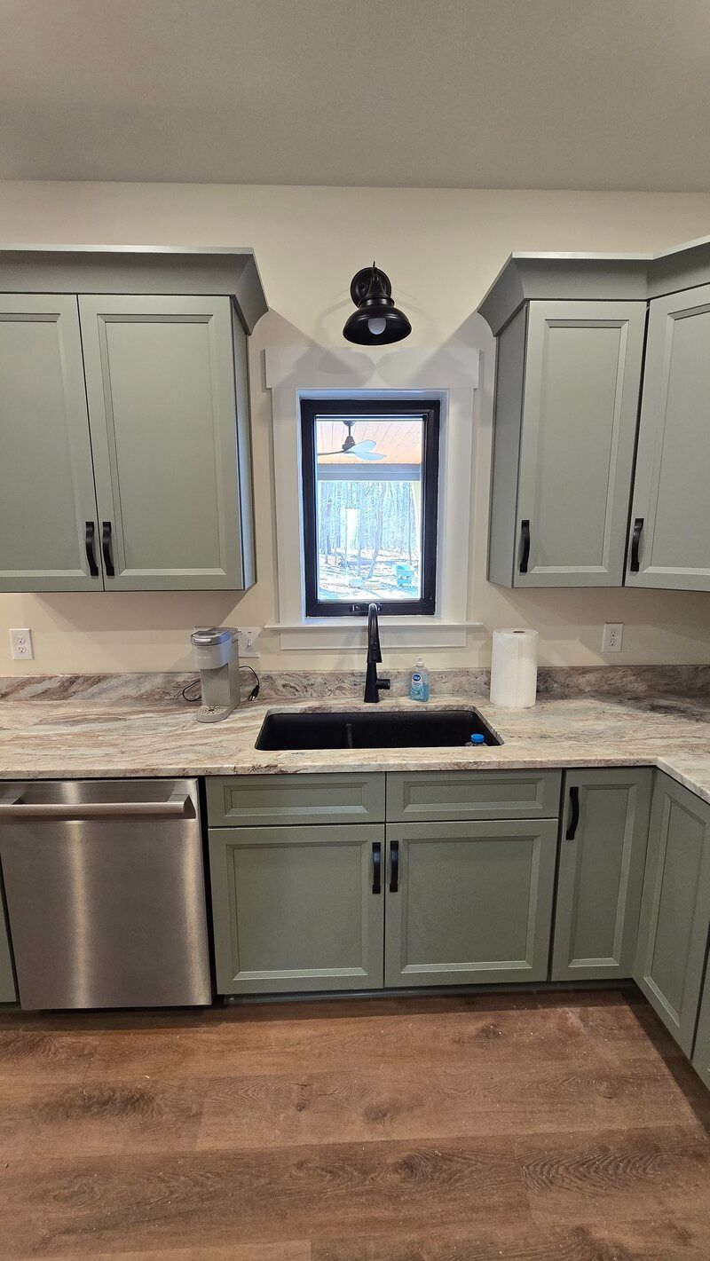 Kitchen with sage green cabinets, black sink and faucet, granite countertops, window.