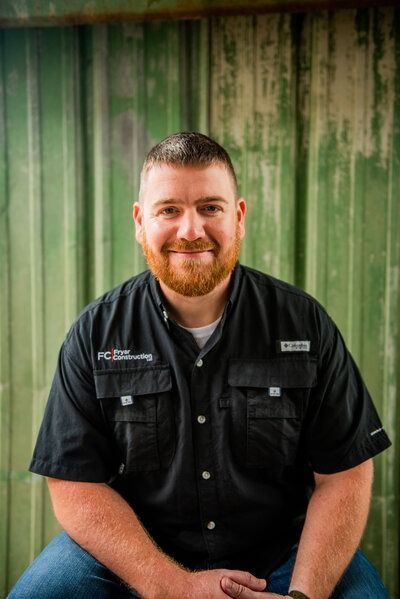 Man with red beard, smiling, wearing a black shirt and jeans, in front of a green wall.