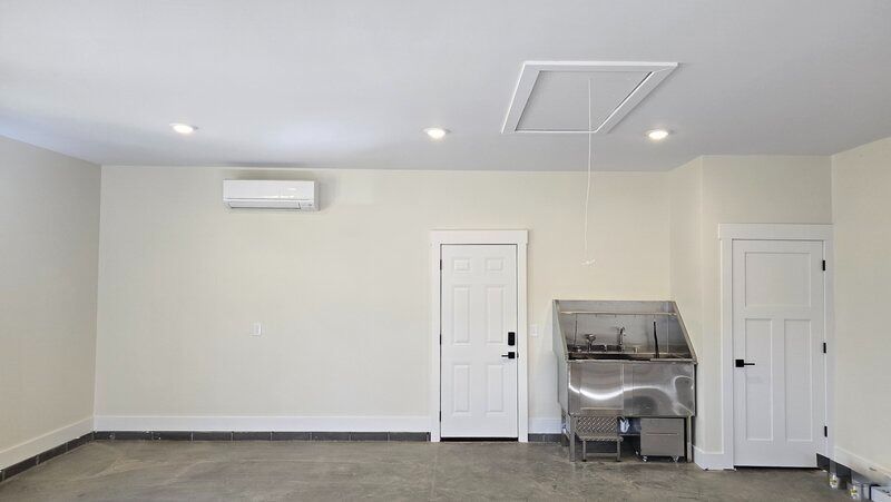 Empty garage interior with a white door, stainless steel utility sink, and recessed lighting.