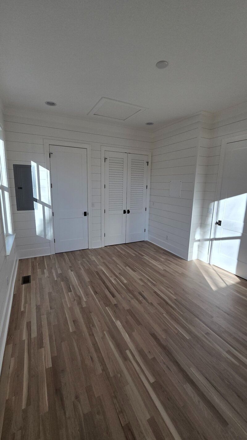Empty room with wood floors and white brick walls. Two doors and a window visible.