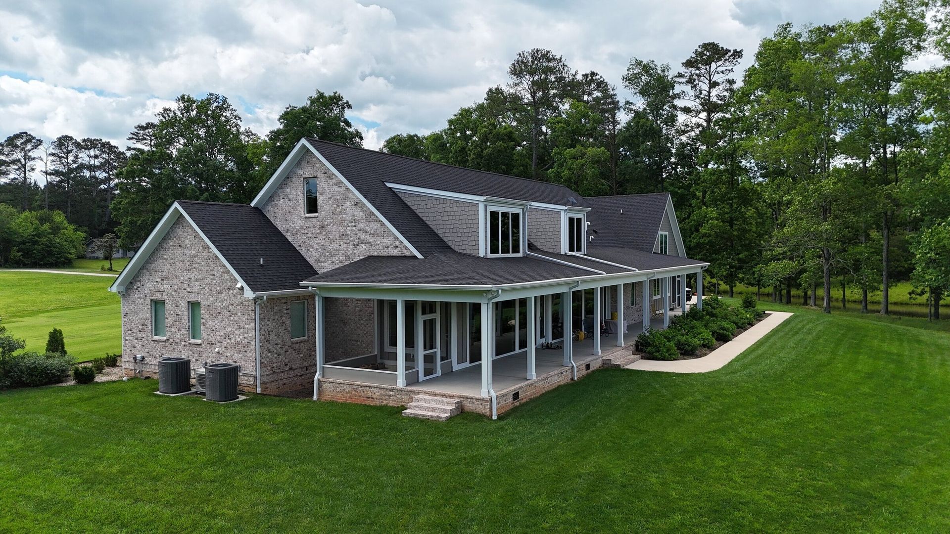 Brick two-story house with a long porch, surrounded by green grass and trees on a sunny day.
