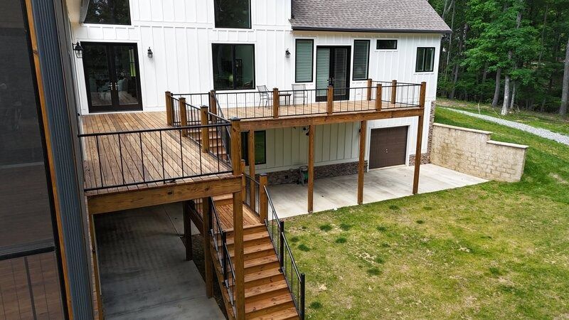 Wooden deck and stairs leading down from a two-story white house with a garage and green yard.