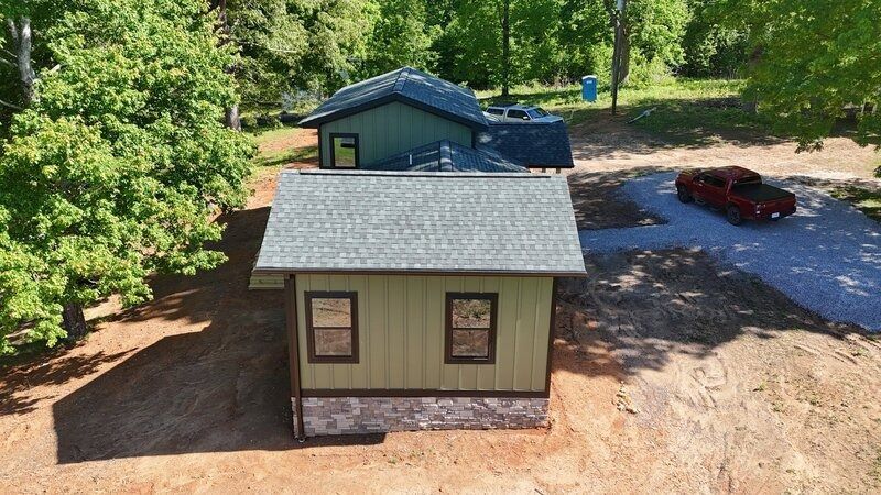 Green-sided cabin with two windows, a gravel roof and driveway, and a red truck.