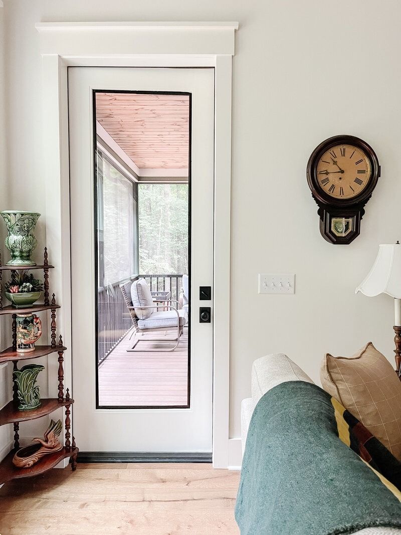 White door with glass panel leading to a screened porch, with a clock on the wall and a small shelf on the left.