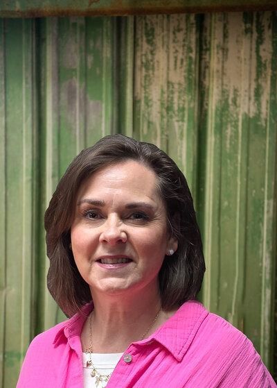 Woman in a pink shirt smiles in front of a weathered green background.