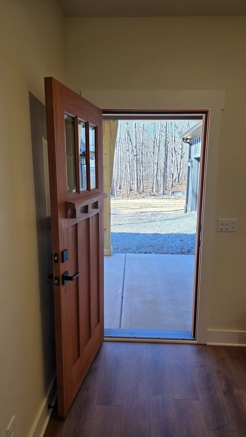 Open wooden door with glass panels leads to a concrete patio and a wooded area.