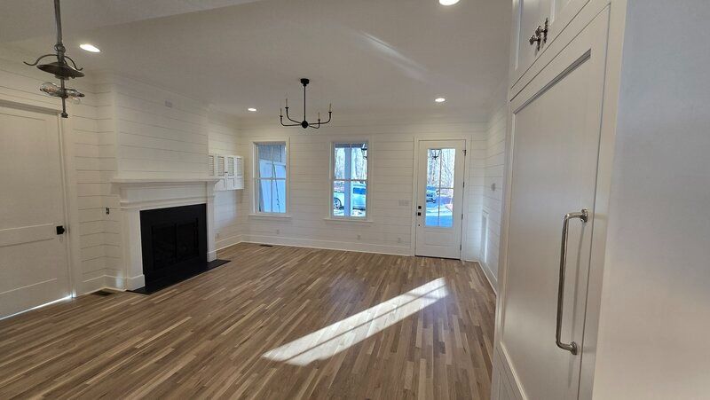 Empty living room with fireplace, three windows, and wood flooring. Bright, white walls and trim.