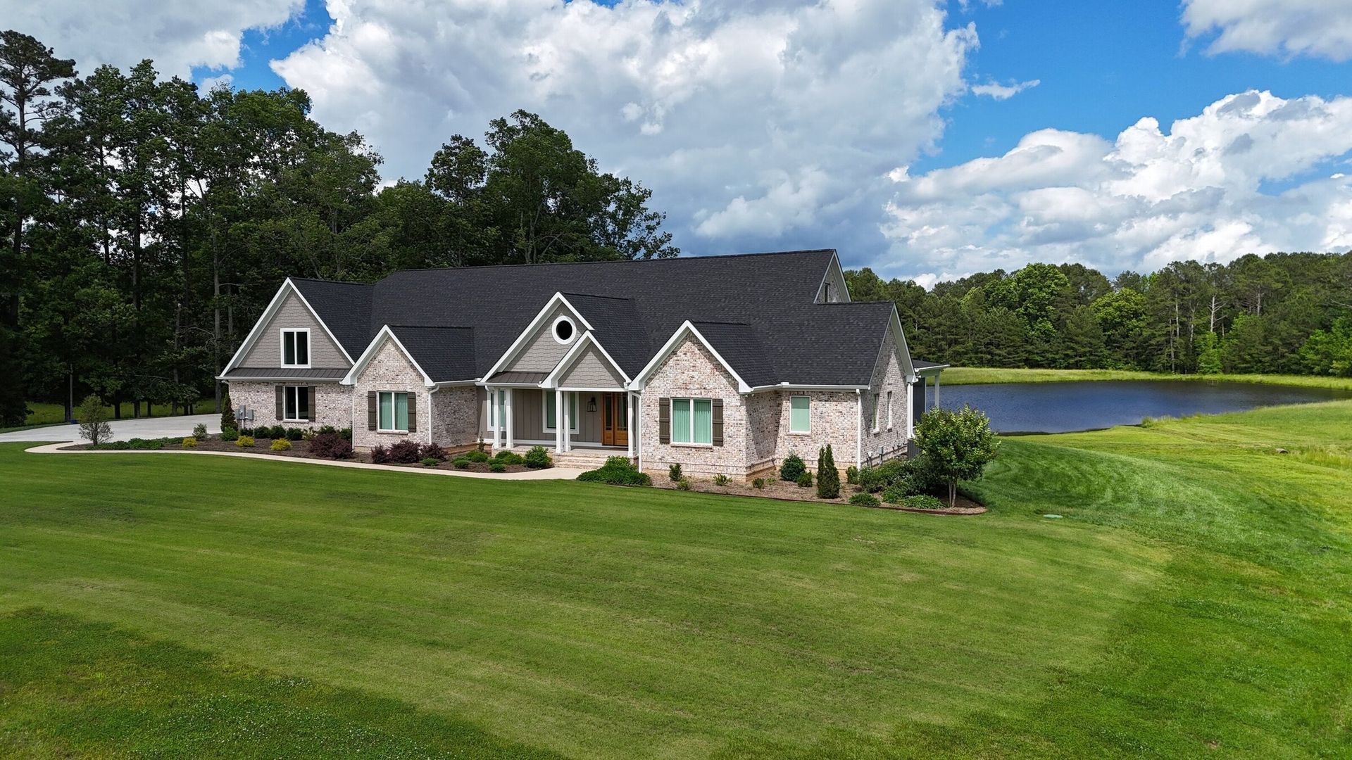 House with gray roof, brick and siding exterior, fronting a lake, on a grassy lawn under a blue sky.
