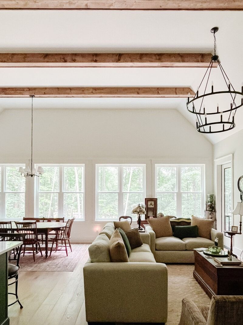 Spacious living room with wood beams, large windows, dining table, and two sofas.