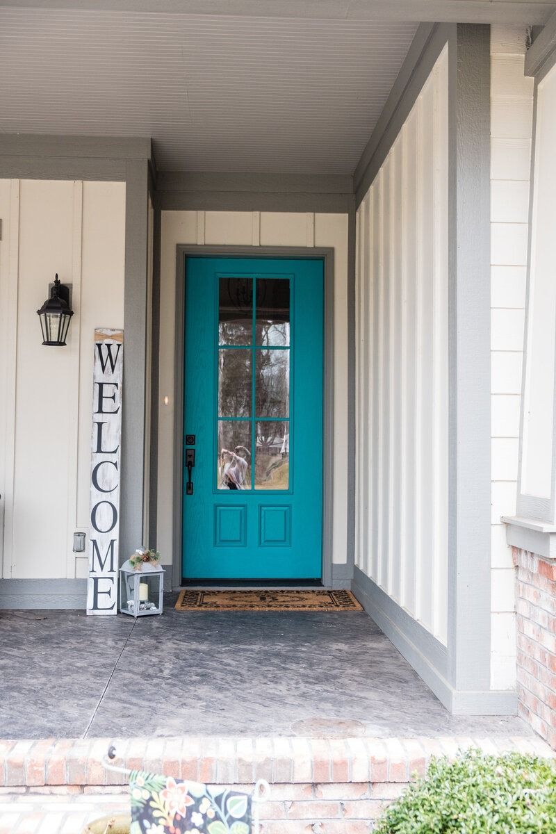 Teal front door with glass panes under a gray porch roof. 