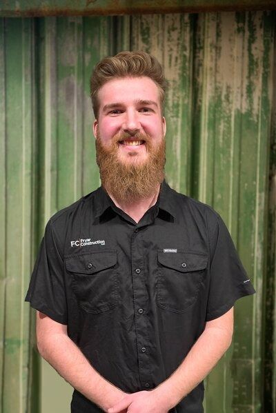 Man with a beard in a black shirt, smiling in front of a green wall.