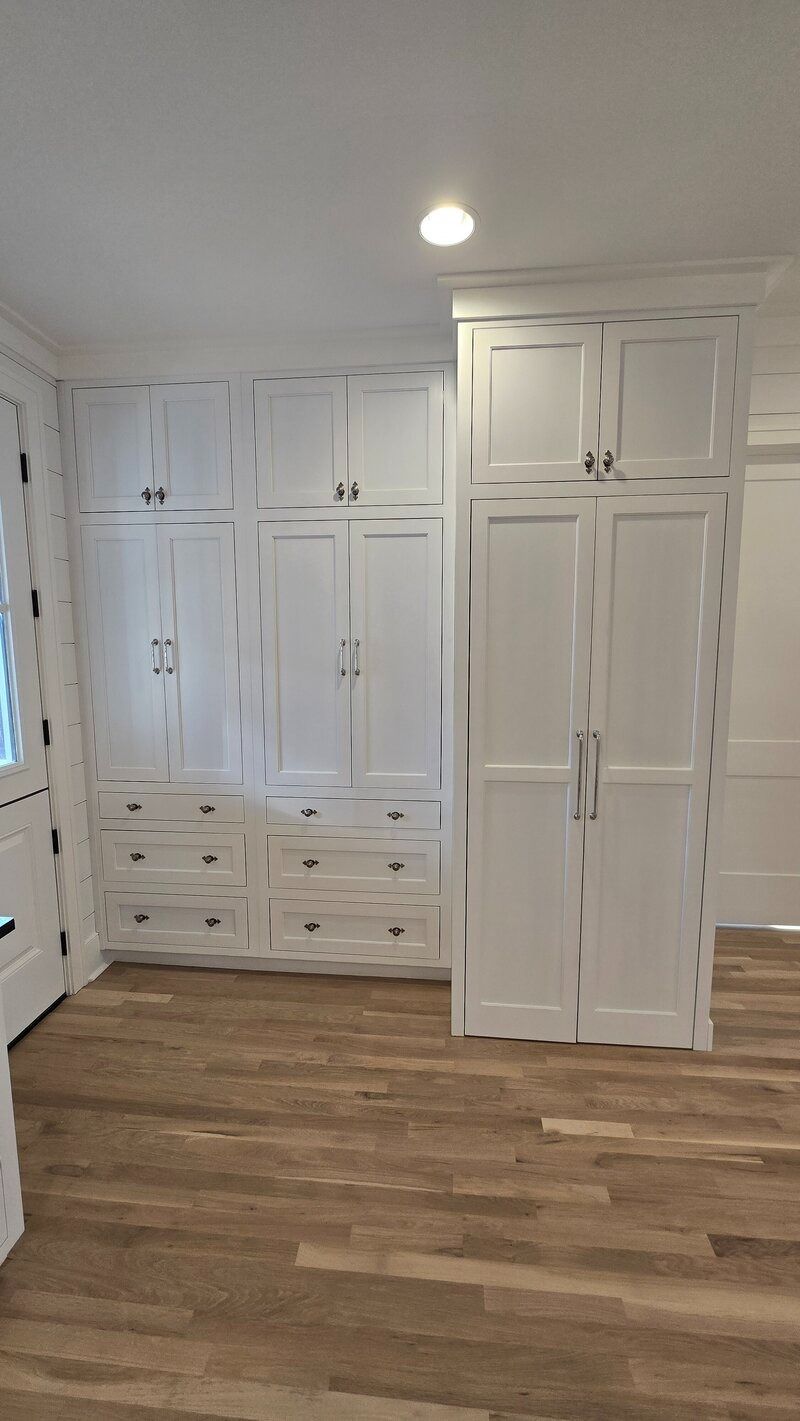 White built-in storage cabinets against white walls with hardwood flooring.