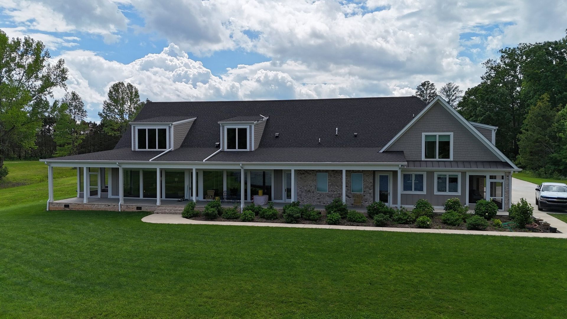 Large gray house with stone accents, a covered porch, and a well-manicured lawn under a cloudy sky.