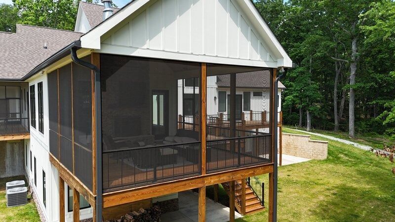 Screened-in porch on a two-story home with a wooden deck, overlooking a grassy yard and trees.
