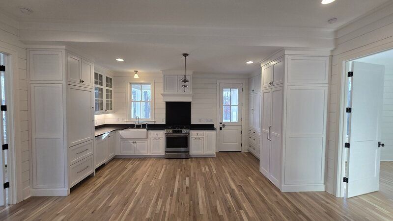 White kitchen with wooden floors, black countertops, and cabinetry.