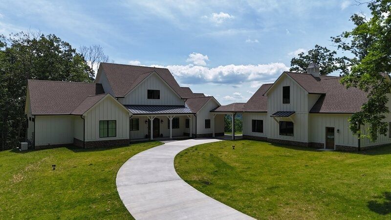 White farmhouse with a curved driveway on a grassy lawn under a blue sky.
