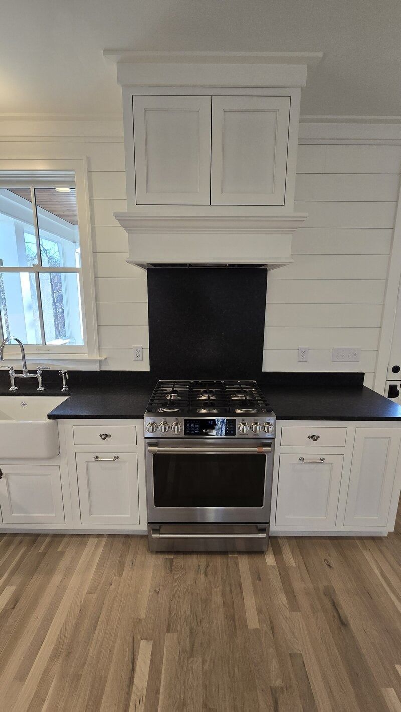 White kitchen with stainless steel oven, black countertop, and white cabinets.