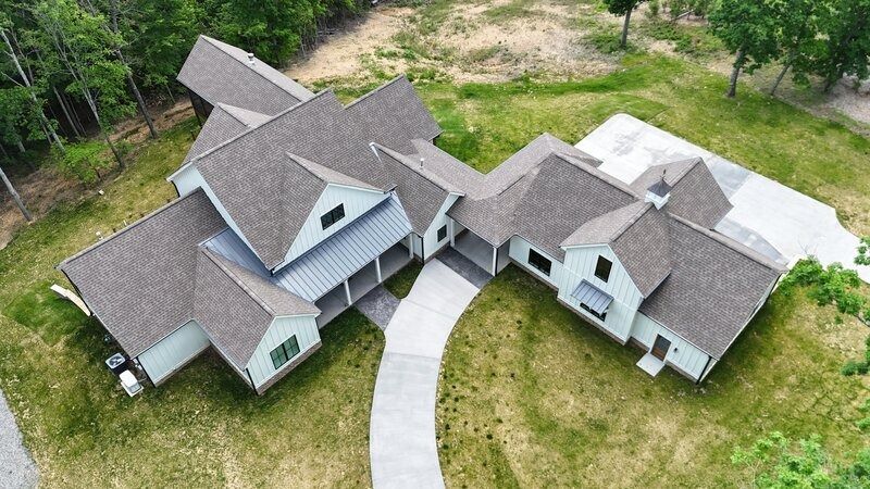 Aerial view of a modern white house with a gray roof and a winding concrete driveway.