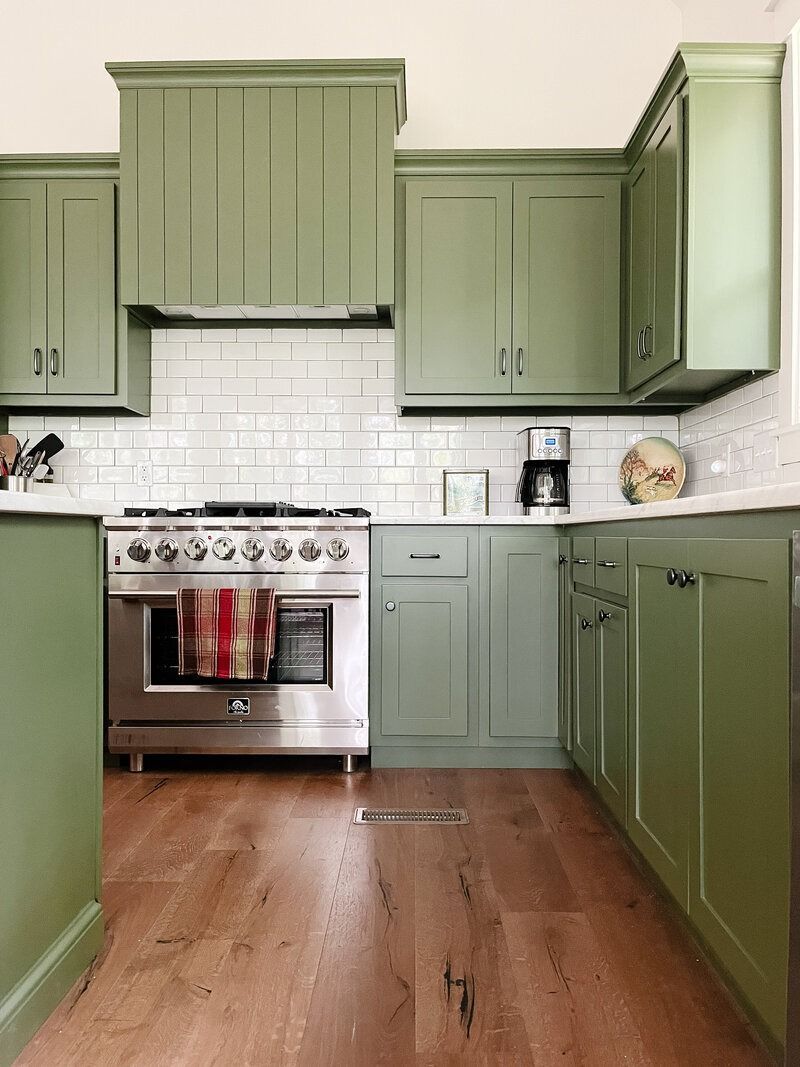 Green kitchen cabinets with stainless steel appliances and wood flooring.