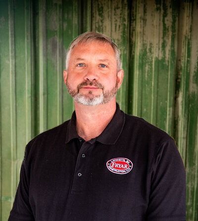 Man with graying beard in black shirt smiles, standing in front of a green background.