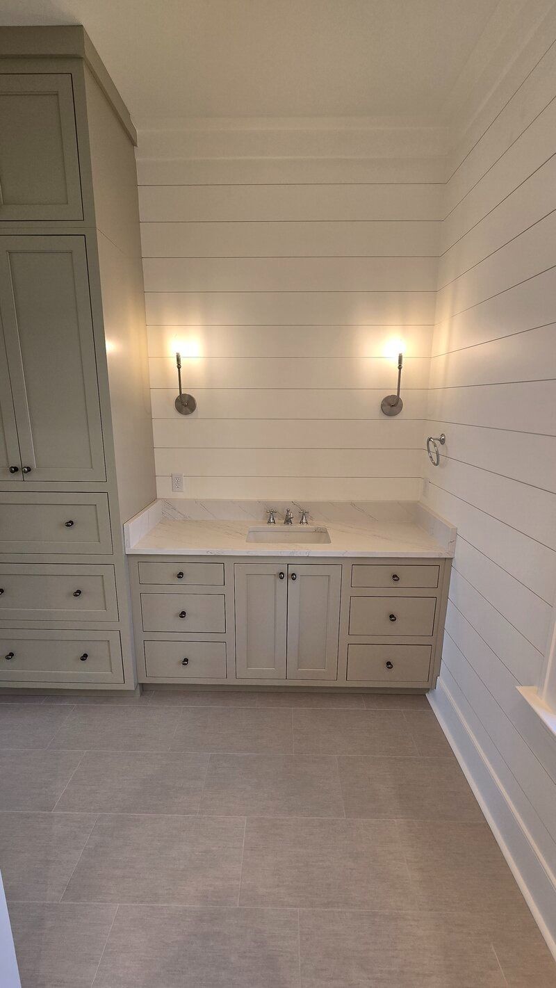 Bathroom with light gray cabinets, white countertop, sconces, and shiplap walls.