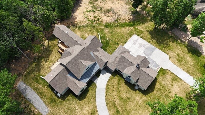 Aerial view of a modern house with a complex roof, driveway, and surrounding trees.