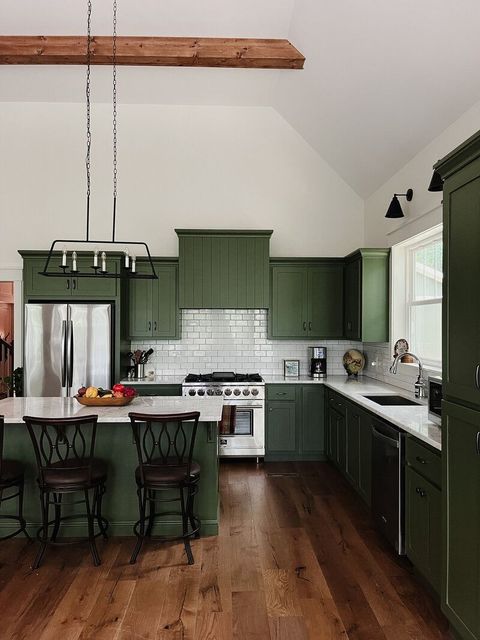 Green kitchen cabinets, stainless steel oven, white backsplash, and wooden floors.