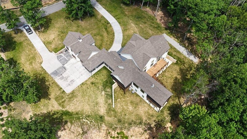 Aerial view of a large white house with a brown roof and long driveway surrounded by green trees.