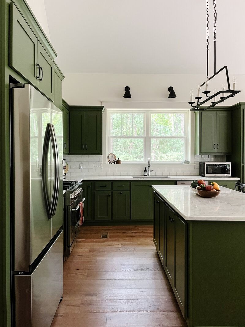 Green kitchen with stainless steel appliances, white countertops, and wooden floors.
