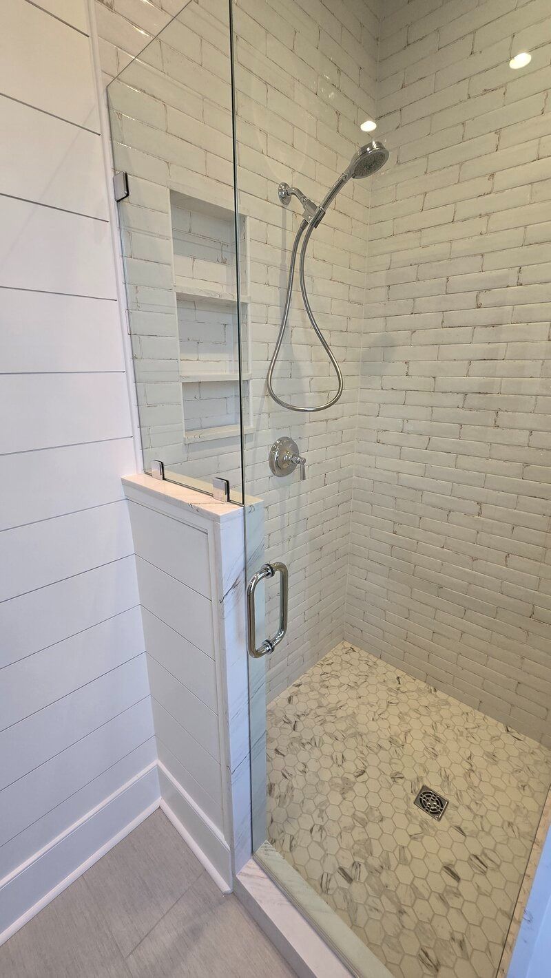 Modern shower with glass door, white brick tile walls, built-in bench, and shower head.