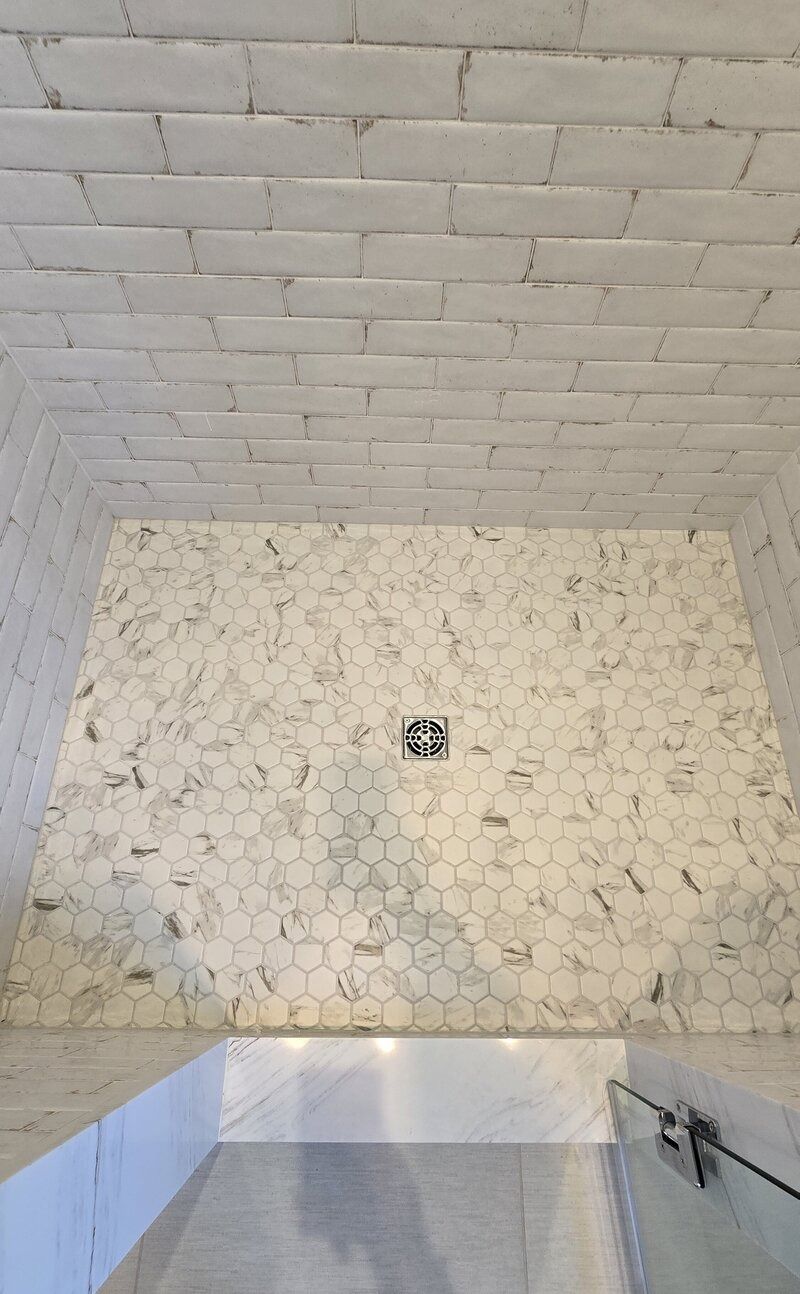 White tiled shower with a glass door, hexagon tile floor, and brick-like tile walls.