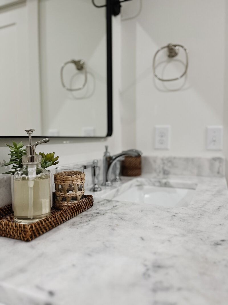 Bathroom countertop with soap dispenser, decorative tray, sink, and mirror reflection.