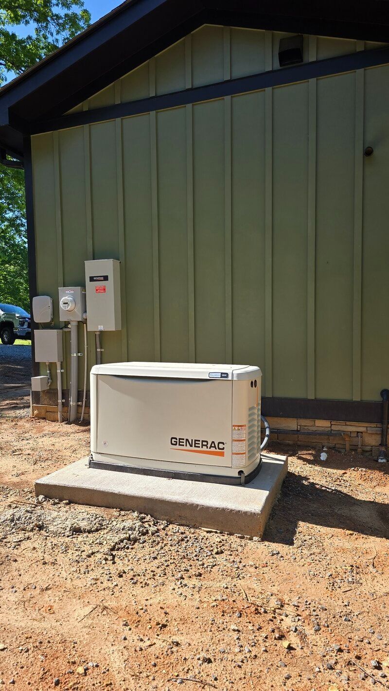 A generator on a concrete pad near a building with electrical boxes. The building has green siding.