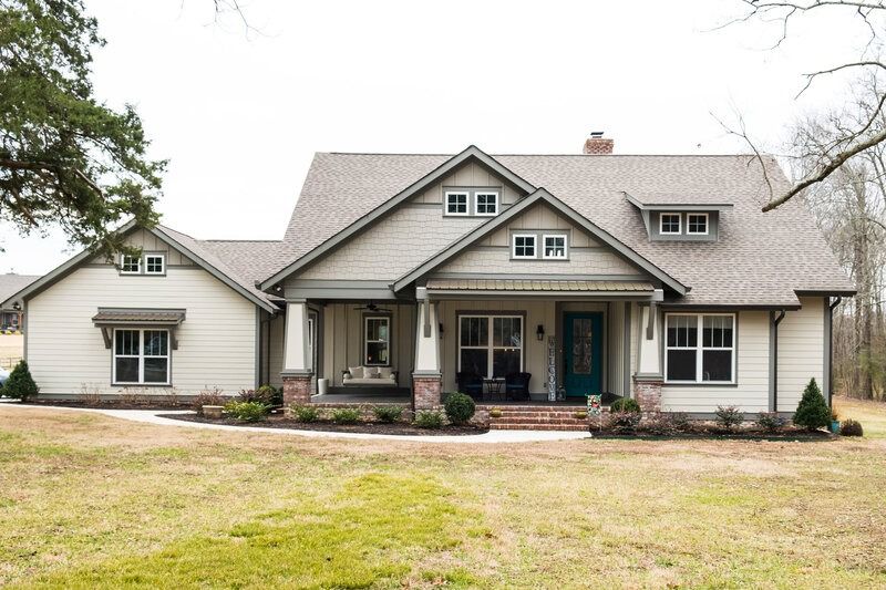 Tan house with teal door, porch, and gray roof, in a grassy yard.
