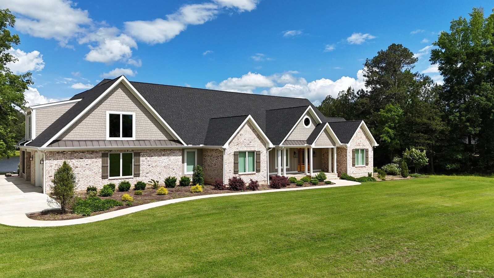 Large brick house with a dark roof and manicured lawn under a blue sky.