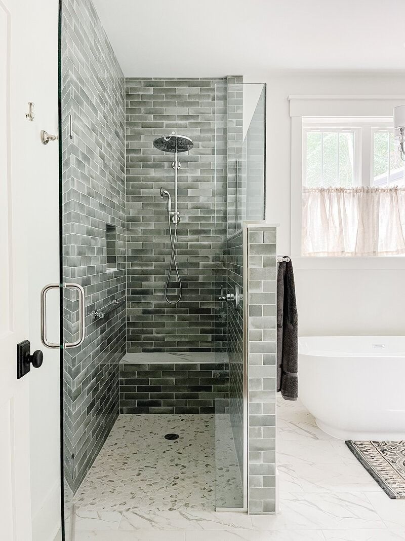 Modern bathroom with glass-enclosed shower featuring gray brick-like tile, bench, and terrazzo floor.