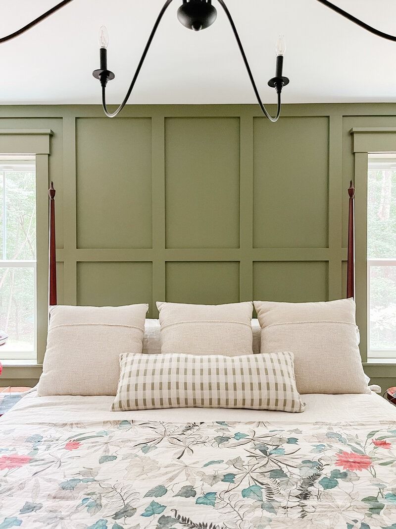 Green paneled accent wall behind a bed with beige pillows and a floral patterned bedspread.