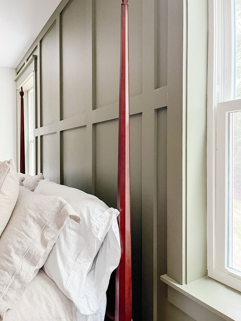 Bedroom with olive green wall paneling, a wooden bedpost, and a window with white trim.