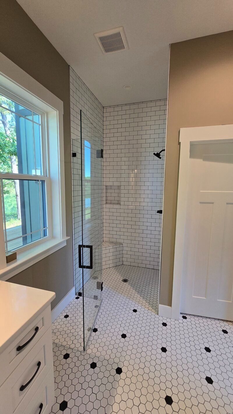 Bathroom with white and black patterned floor, white tile shower, and glass door.