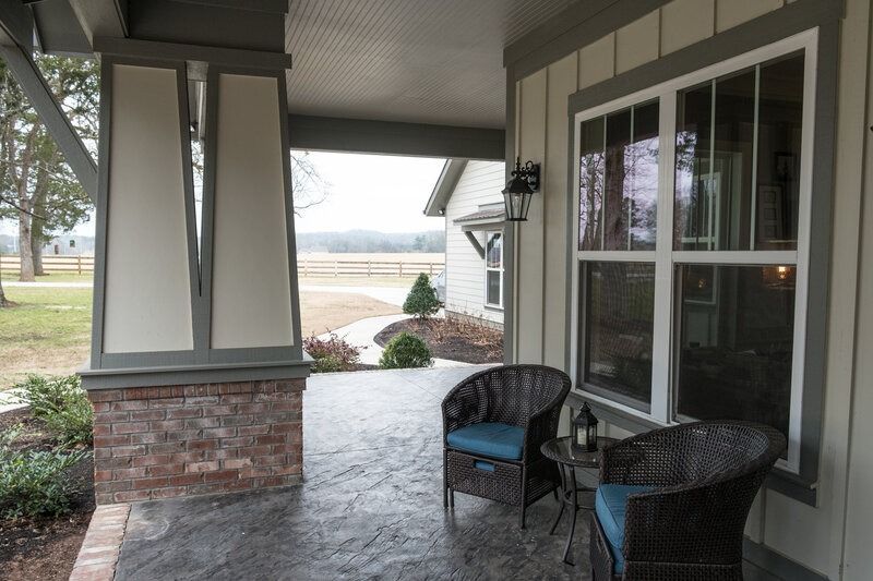 Covered porch with wicker chairs, brick column, and view of a field.
