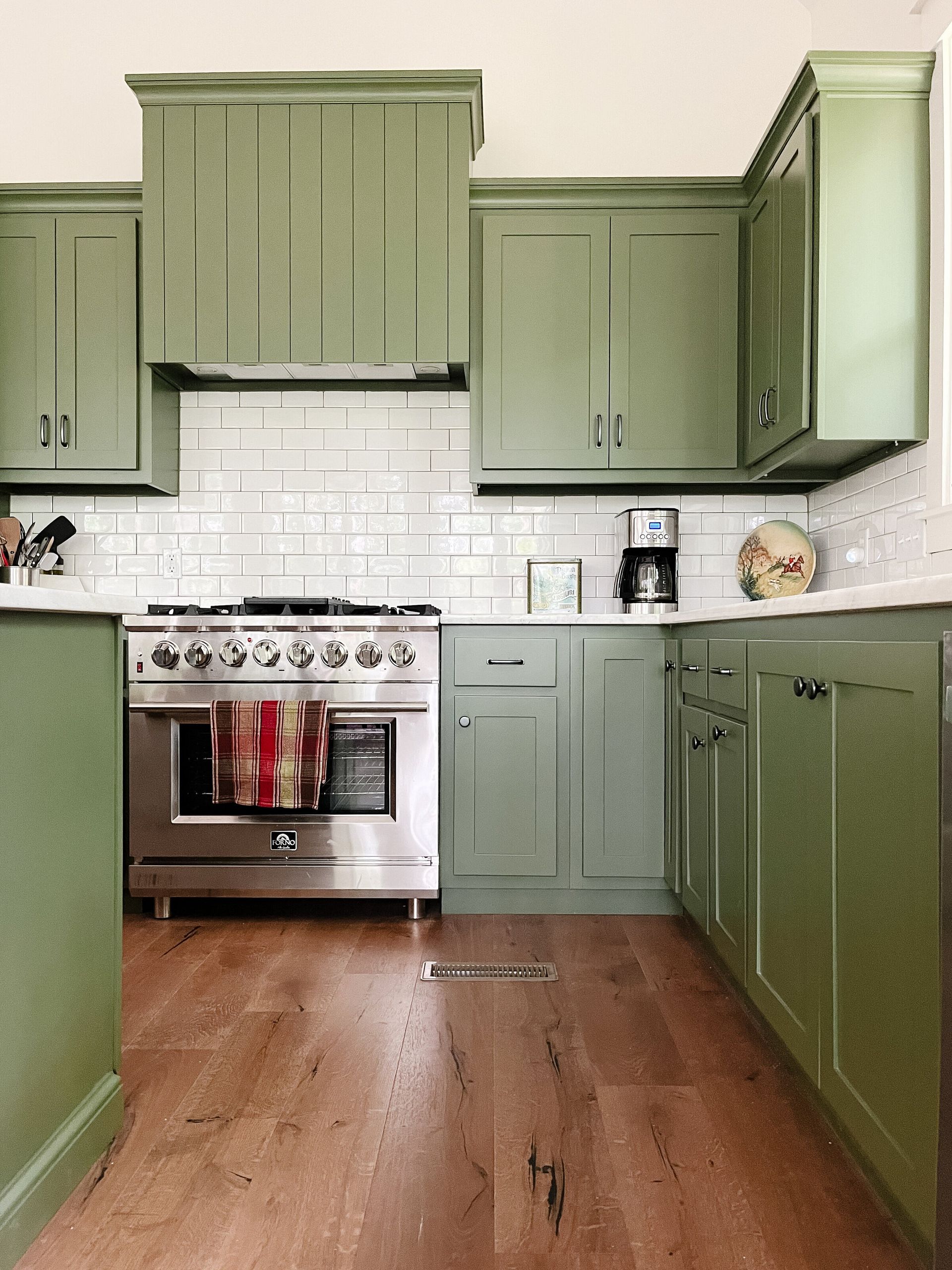 Green kitchen with stainless steel appliances, white subway tile backsplash, and wood floors.