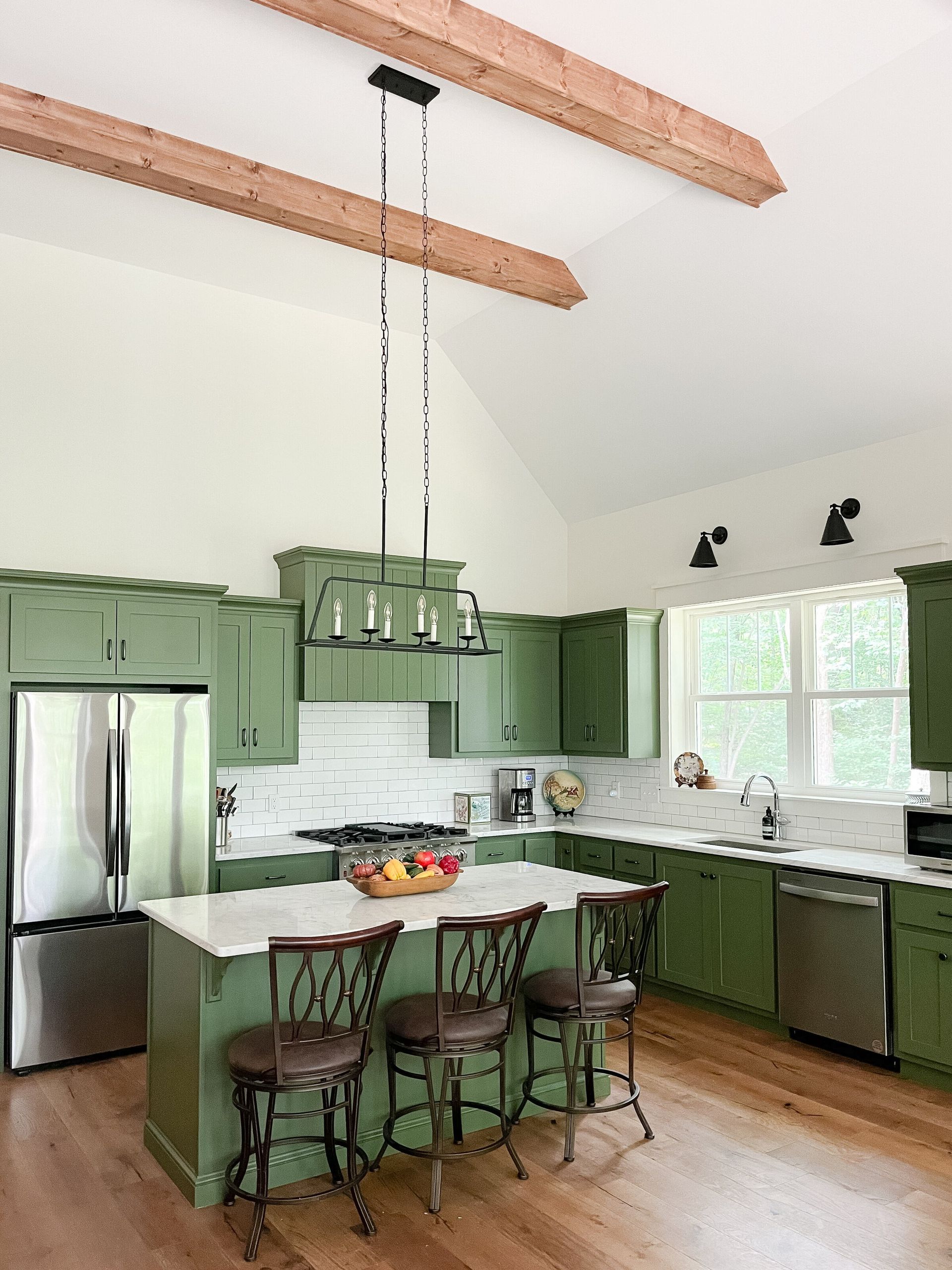 Green kitchen with stainless steel appliances, white countertops, and wood beams.